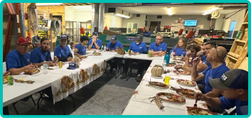A group of people wearing blue shirts sit around tables in a large room, enjoying a meal together while discussing careers and new job opportunities.